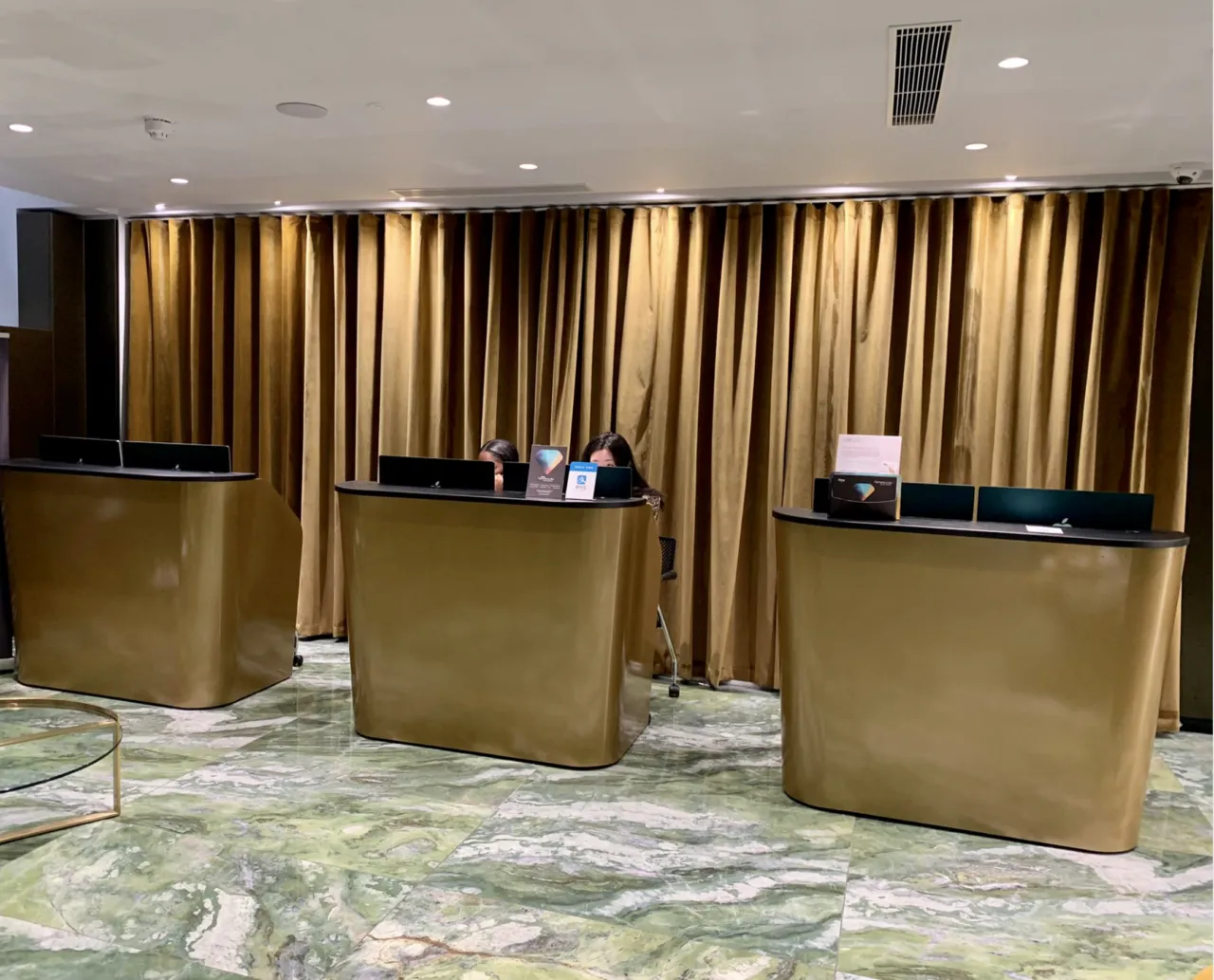 Three gold-colored curved counters stand on a green marbled floor in front of a long backdrop of gathered gold curtains.